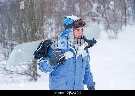 Portrait d'un snowboardeur sur une pente enneigée. Freerider avec un snowboard dans un chapeau et un masque de montagne Banque D'Images