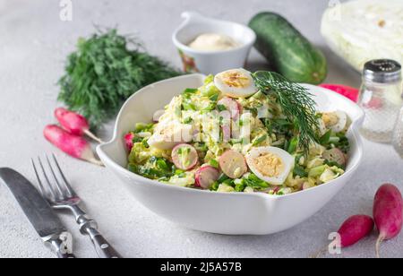 Salade de chou chinois, concombre, radis, ciboulette et œufs de caille dans une assiette blanche sur fond gris Banque D'Images