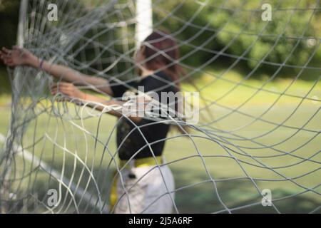 Fille règle le filet à l'objectif de football. La fille est debout sur la porte. Détails du jeu sportif. Écolière dans le stade. Filet sur porte. Banque D'Images