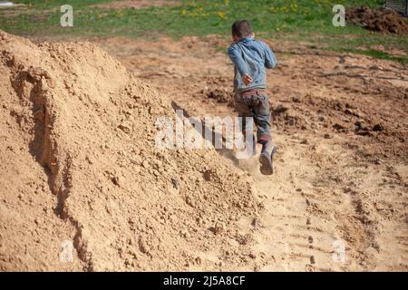 Le garçon est allongé dans le sable. Le gamin est sale vêtements. Le garçon est tombé dans le bac à sable. Enfant méchant s'amuser. Un enfant sans mouvement après la chute. Banque D'Images