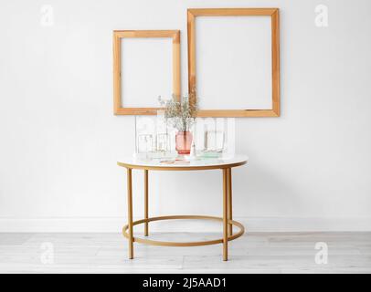 Bijoux élégants, vase avec fleurs sur la table et cadres blancs dans la chambre Banque D'Images