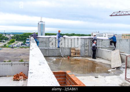 Kemerovo, Russie - 24 juin 2021. Sur le toit des ouvriers du bâtiment tirent le maillage de construction de protection de fausse façade qui protégera les constructeurs Banque D'Images
