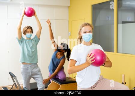 Adolescents dans les masques d'entraînement pilates dans la salle de gym avec entraîneur Banque D'Images