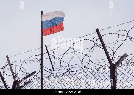 Vue du drapeau russe derrière le fil barbelé contre le ciel nuageux. Concept de sanctions anti-russes. Un poste frontalier à la frontière de la Russie. Annuler la culture russe Banque D'Images