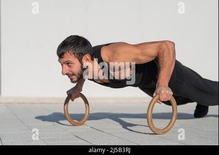 Un homme en noir sportswear faisant des anneaux push-up à l'extérieur. Banque D'Images