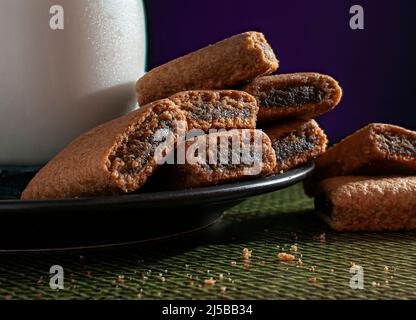 Barres à biscuit de la Fig une assiette noire avec un verre de glace ou de lait froid, sur un linge de table vert avec un rouge violet foncé Banque D'Images