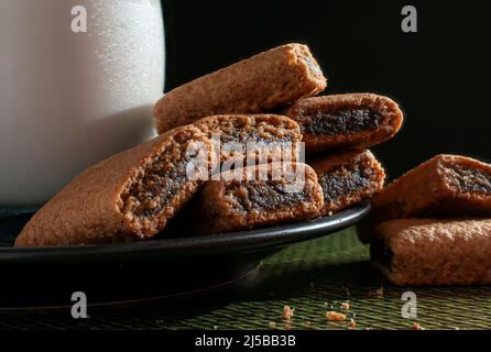 Barres de biscuit de Fig une assiette noire avec un verre de glace ou de lait froid, sur une nappe verte, avec un fond noir Banque D'Images