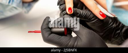 Vernis de manucure. Gros plan d'un maître de manucure portant des gants noirs en caoutchouc appliquant du vernis rouge sur un ongle femelle dans le salon de beauté Banque D'Images