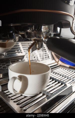 Versez le flux de café de la machine professionnelle dans une tasse. Barista prépare un espresso à l'aide du porte-filtre. Café fraîchement moulu. Boissons grillées bl Banque D'Images