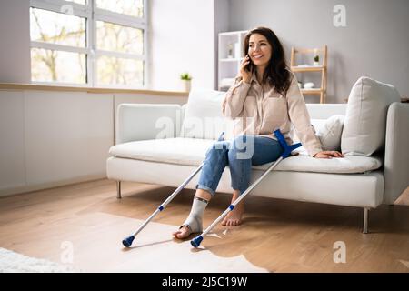 Femme atteinte d'une jambe en utilisant des béquilles à la maison Banque D'Images