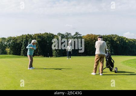 homme asiatique senior jouant au golf à proximité d'amis interraciaux avec bâton de drapeau et voiturette de golf Banque D'Images