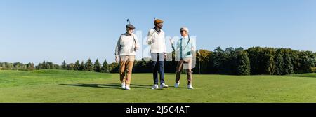des amis interraciaux seniors marchant avec des clubs de golf sur le terrain, bannière Banque D'Images