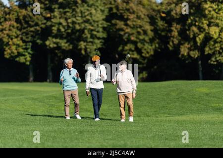 amis séniors interraciaux marchant avec des clubs de golf sur le terrain Banque D'Images