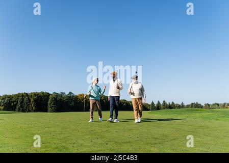 des amis interraciaux seniors marchent avec des clubs de golf sur le terrain Banque D'Images