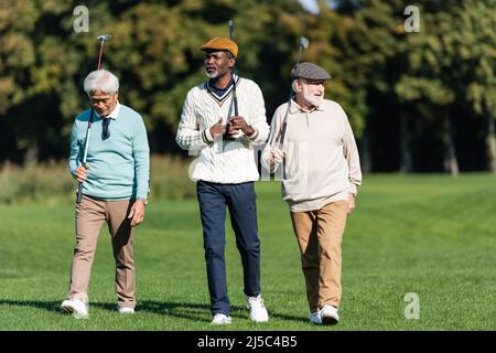 amis séniors interraciaux marchant avec des clubs de golf à l'extérieur Banque D'Images