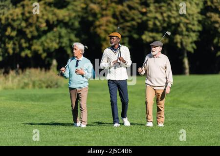 hommes âgés interraciaux marchant avec des clubs de golf sur le terrain vert Banque D'Images