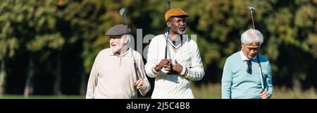 amis séniors interraciaux marchant avec des clubs de golf à l'extérieur, bannière Banque D'Images