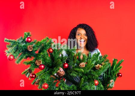 femme afro-américaine achetant un arbre de Noël studio mur rouge Banque D'Images