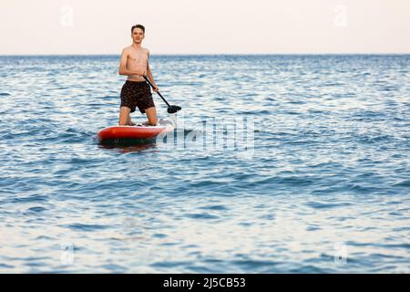 Adolescent apprenant à pagayer sur un panneau SUP dans la mer à genoux Banque D'Images