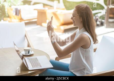 femme blogueuse prenant un selfie tout en étant assise à une table dans un café. Banque D'Images