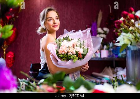 femme blonde gracieuse en tablier vendant des fleurs dans son propre magasin Banque D'Images