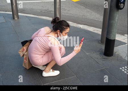 12 mars 2020, Singapour, République de Singapour, Asie - Une jeune femme prend des photos à un feu de circulation piétonnier tout en portant un respirateur pour se protéger contre la contagion du coronavirus pandémique. [traduction automatique] Banque D'Images