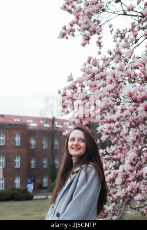 La jeune femme Brunette se trouve près d'un magnifique gros magnolia rose près du château de Wawel à Cracovie, en Pologne Banque D'Images