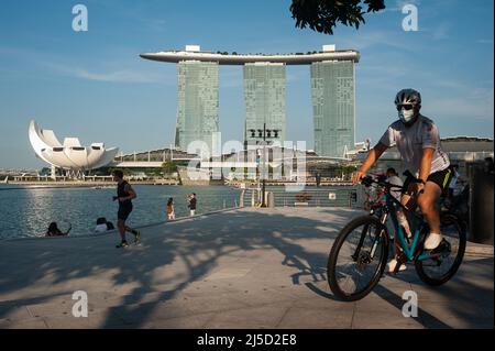 07/24/2021, Singapour, République de Singapour, Asie - Un homme portant un masque fait le tour de son vélo le long des rives de la rivière Singapour pendant la crise de Corona en cours, tandis que l'hôtel Marina Bay Sands est vu en arrière-plan. La cité-État d'Asie du Sud-est est revenue à un niveau d'alerte plus élevé avec des mesures de verrouillage plus strictes après que le nombre d'infections par le virus Covid-19 a de nouveau augmenté. [traduction automatique] Banque D'Images