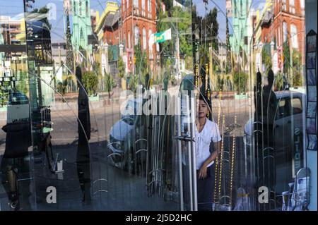 16.12.2013, Yangon, Myanmar, Asie - Une femme se tient derrière une porte vitrée d'un magasin au centre de l'ancienne capitale où se reflète une scène de rue. [traduction automatique] Banque D'Images