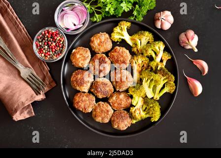 Côtelettes maison et brocoli frits sur plaque sur fond de pierre noire. Vue de dessus, plan d'appartement Banque D'Images