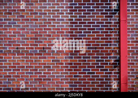 Mur de briques avec briques dans les tons de rouge de l'orange au violet. Le tuyau de caniveau rouge traverse la brique pour offrir un contraste. Banque D'Images