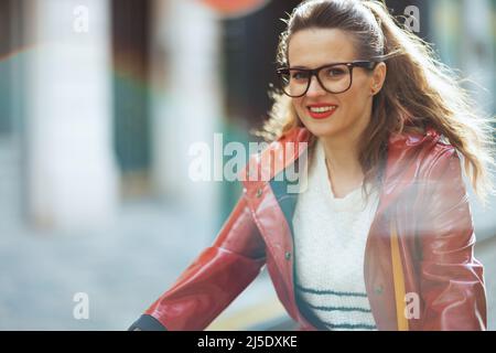 heureuse femme élégante en manteau de pluie rouge dehors sur la ville rue à vélo. Banque D'Images