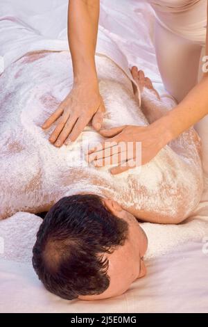 Une femme guérisseur exécute un rituel avec du sel, frotte le dos d'un homme couché avec du sel. Détente. Banque D'Images