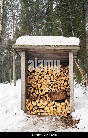 Un stockage de bois de chauffage avec un panier en osier pour transporter du bois, dans une forêt de sapins enneigés. Banque D'Images