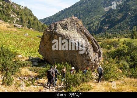Groupe de randonneurs passant par un grand rocher glaciaire erratique dans la vallée des lacs Urdini, montagne Rila, Bulgarie Banque D'Images
