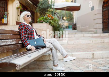 Élégante femme à la retraite assise à l'extérieur de la ville Banque D'Images