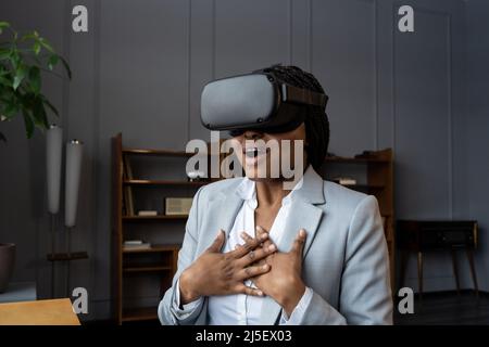 Une femme d'affaires africaine choquée sur le micro-casque VR immergée dans le monde virtuel de 3D hurle Banque D'Images