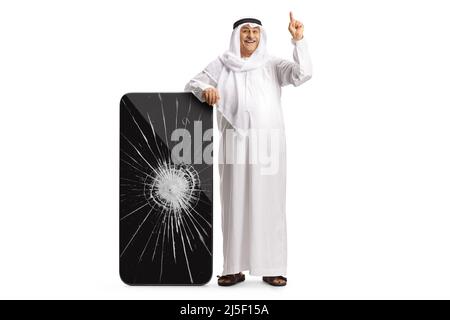 Portrait complet d'un arabe penché sur un grand téléphone intelligent avec écran fissuré et pointant vers le haut isolé sur fond blanc Banque D'Images