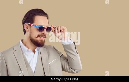 Beau homme en costume et lunettes de soleil avec motif drapeau américain sur fond beige espace copie Banque D'Images