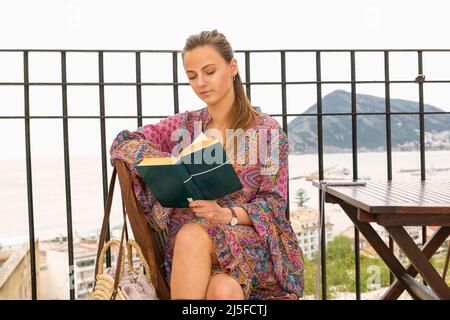 une jeune femme assise sur une terrasse au bord de la mer lisant un livre Banque D'Images