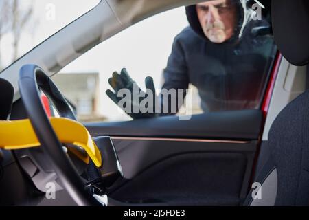 Voleur d'homme regardant à travers la fenêtre au verrouillage manuel du volant dans la voiture Banque D'Images