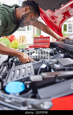 Homme travaillant sous le capot d'une voiture fixant le moteur à l'aide d'une clé Banque D'Images