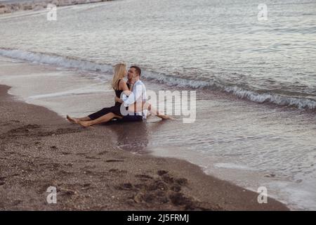 Adorable couple embrassant tout en étant assis sur le sable près de l'océan Banque D'Images