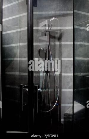 Douche de luxe minimaliste, entièrement décorée avec des carreaux gris foncé, avec une pomme de pluie Banque D'Images