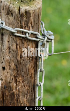 Une chaîne métallique lourde enroulée autour d'un poteau de clôture électrique en bois dans un pâturage dans la campagne Banque D'Images