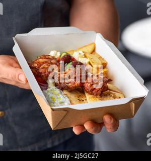 Livraison rapide de la nourriture. Souvlaki grec, salade et gyros à emporter. Menu, servi dans un bac en papier recyclable entre les mains du chef. Banque D'Images