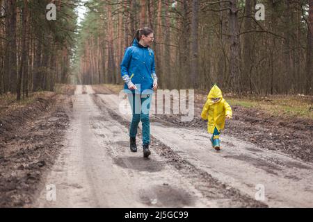 Maman et enfant courant le long de la route forestière après la pluie en imperméable ensemble Banque D'Images