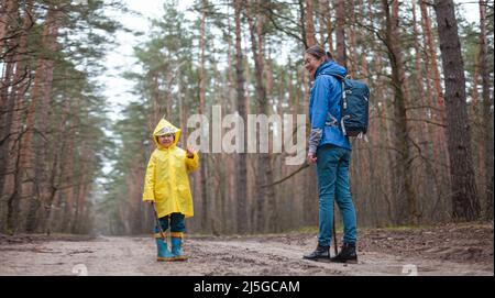 Maman et enfant marchent dans la route forestière après la pluie en imperméable ensemble Banque D'Images