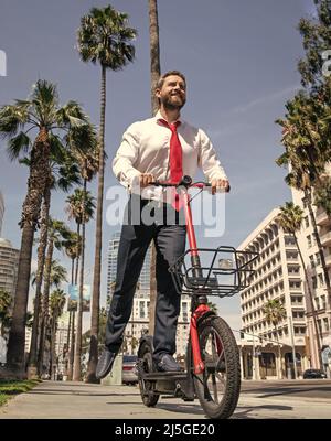 Un gars heureux en tenue de formalwear scooter électrique sur le trottoir, le démarrage Banque D'Images