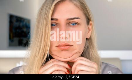 Deuxième menton, obésité. Un portrait d'une femme de 30 ans tirant la peau sur son menton regarde dans l'appareil photo avec un aspect frustré. Problèmes de Banque D'Images